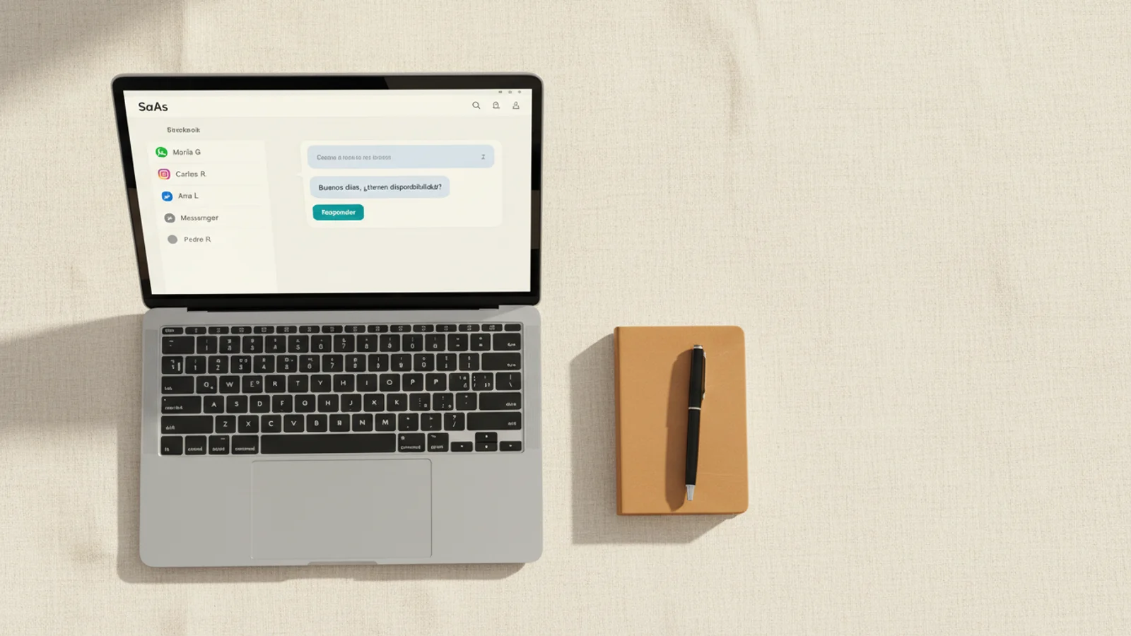 Top-down de MacBook sobre lino crema con bandeja de chats multicanal y libreta de cuero al lado.